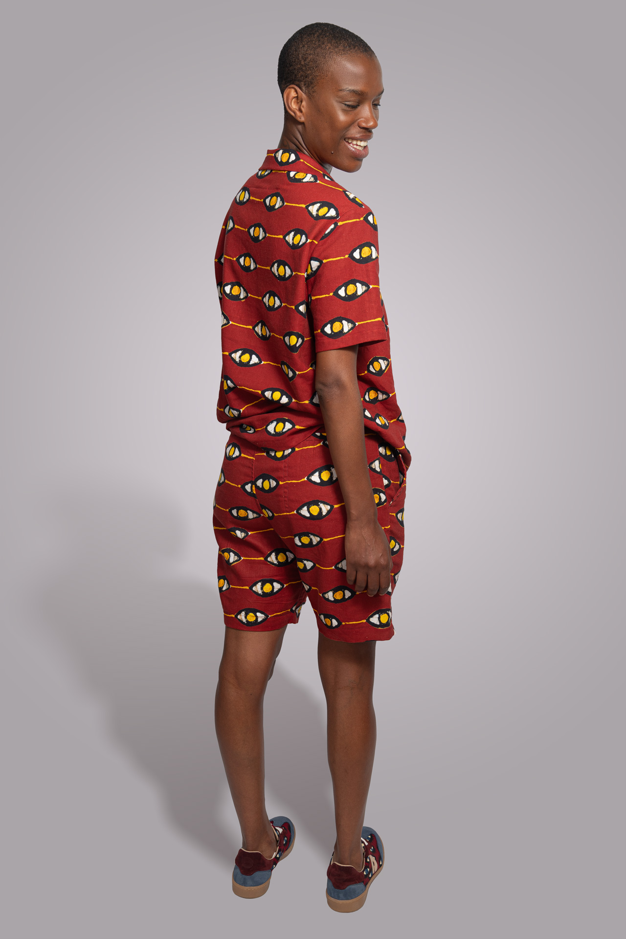 Mujer de espaldas sonriendo con un conjunto africano rojo con estampado de ojos